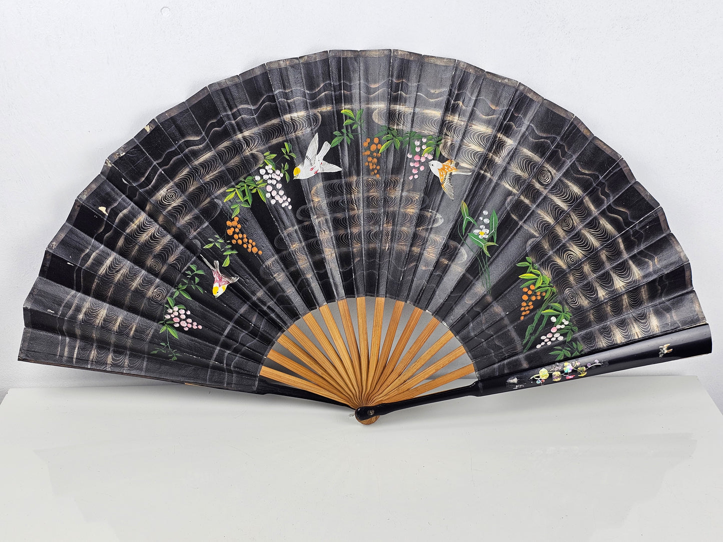 Black hand fan with floral and bird designs on a black background