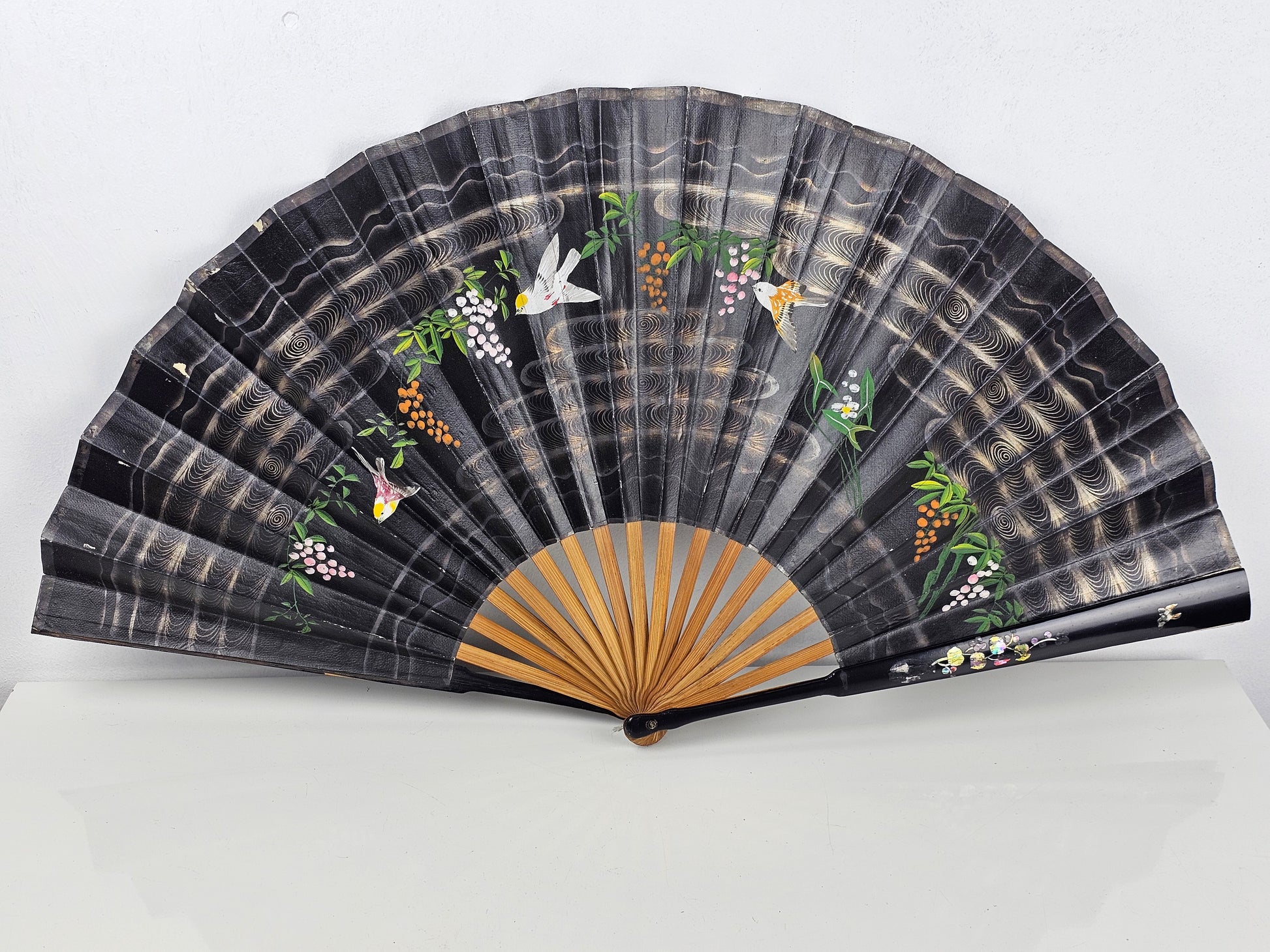 Black hand fan with floral and bird designs on a black background
