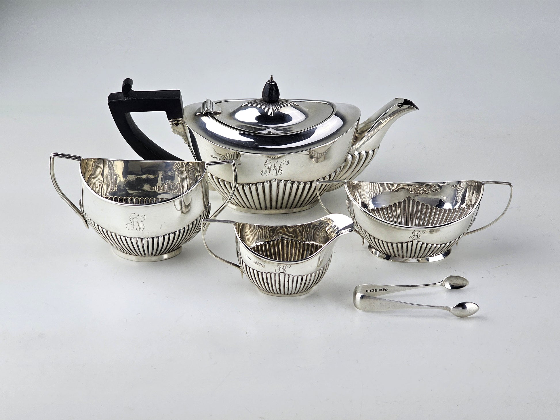 Silver tea set with teapot, sugar bowl, milk jug, and two spoons on a light gray background