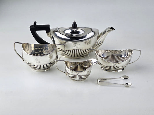 Silver tea set with teapot, sugar bowl, milk jug, and two spoons on a light gray background